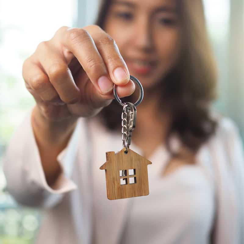Woman holding new home key with wooden house keychain.